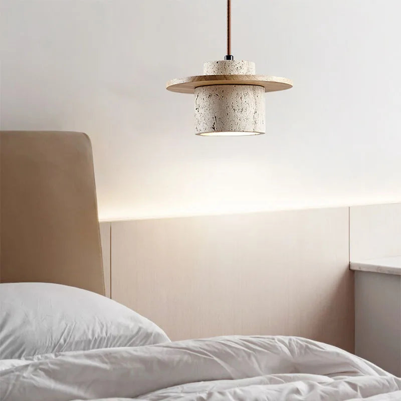 Luminária Pendente Hano em travertino natural com disco de madeira clara, acesa sobre a cama do quarto